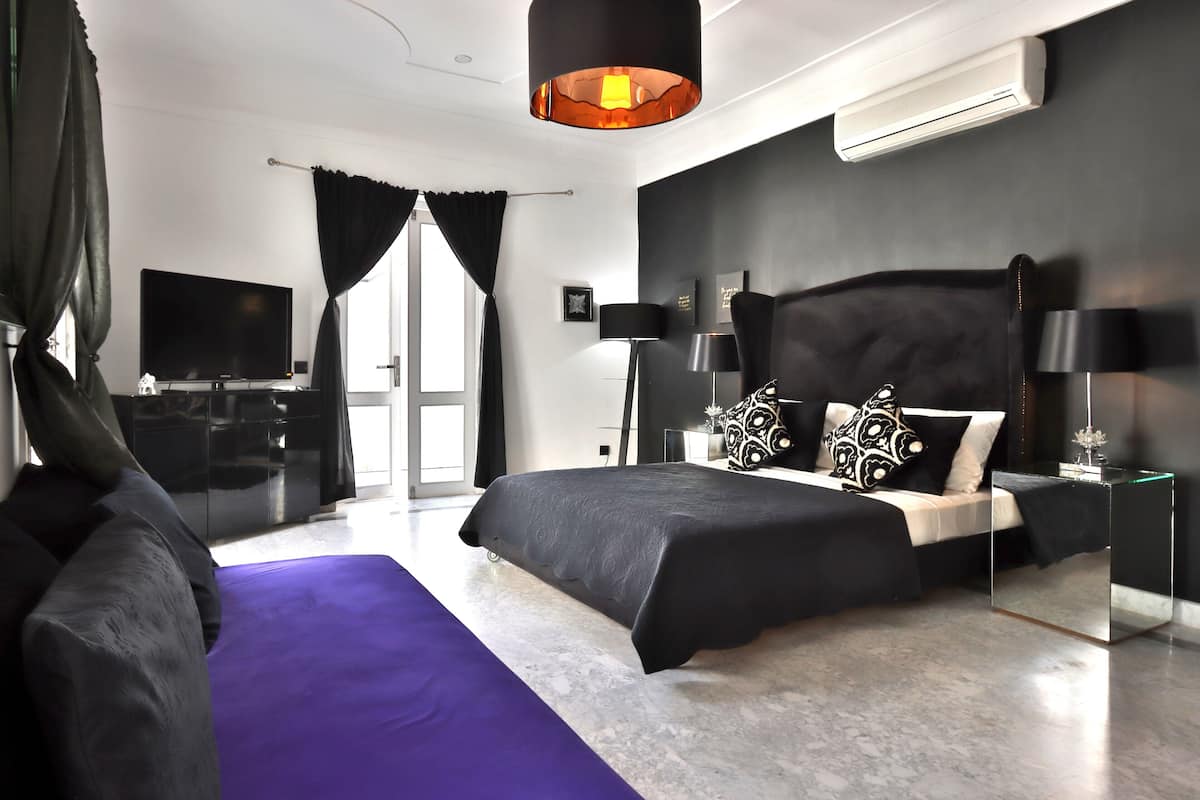 A modern bedroom with a large bed, a flat-screen TV, and a large window with black curtains.