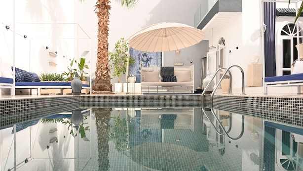 A swimming pool with a glass barrier, a sunbed, a lounge chair, and a palm tree. - Riad VIP (Marrakech)