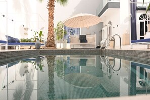 En pool med en glasvägg, en solstol, en fåtölj och en palm.