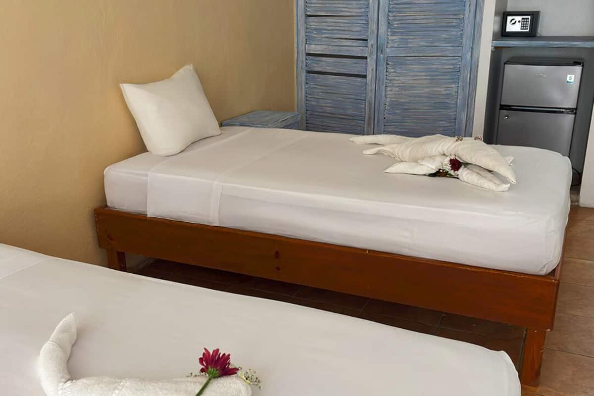 Habitación de hotel con dos camas, cabecera de madera, minibar y un cuadro en la pared.