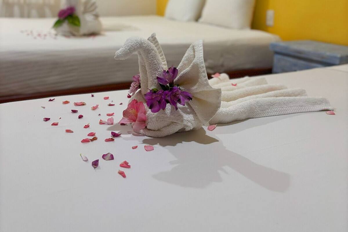 Habitación de hotel con dos camas, una pared amarilla y un cisne decorativo sobre la cama.