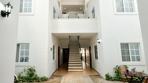 Un edificio de varios niveles con una escalera central, paredes blancas y numerosas ventanas.