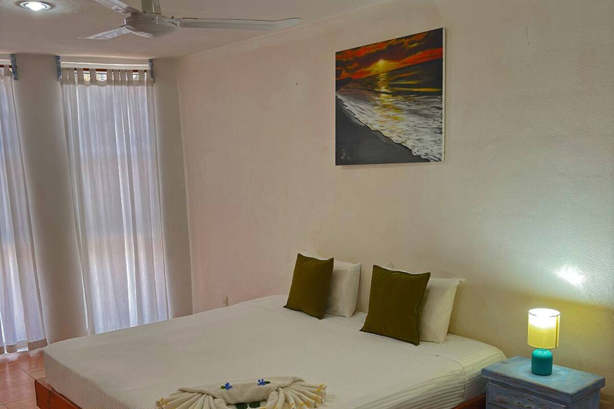 Una cama bien hecha con una presentación de toallas, una mesita de noche con una lámpara y un cuadro en la pared.