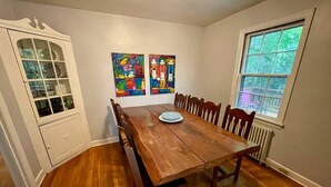 A dining room with a wooden table and chairs, a cabinet with glass doors, and two colorful paintings on the wall.