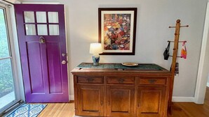 A wooden cabinet with a lamp on top, a purple door, and a framed painting on the wall.