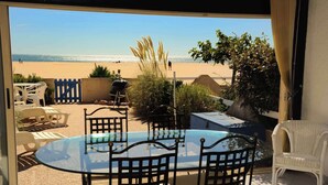 A patio with a glass table and chairs, overlooking a beach.