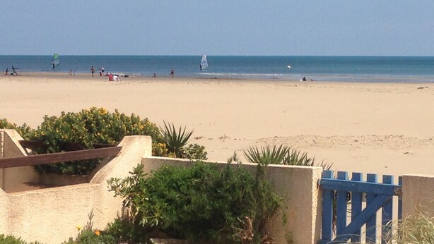 A beach with a sandy shore, a few people, and a sailboat in the distance.