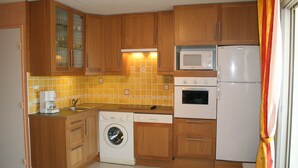 A compact kitchen with wooden cabinets, a washing machine, a microwave, and a refrigerator.