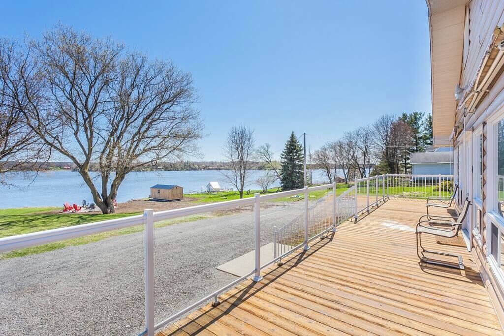 A wooden deck with a railing overlooking a lake, a small shed, and a building with a balcony.