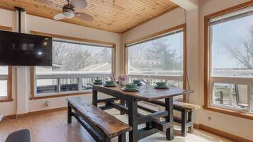 A dining area with a wooden table and benches, large windows, and a ceiling fan.