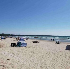 Een strand met tenten en strandstoelen, mensen in het water, en een heldere lucht.