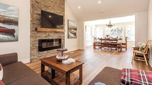 Un salon spacieux doté d’une cheminée en pierre, d’un téléviseur à écran plat et d’un coin repas avec une table et des chaises en bois.