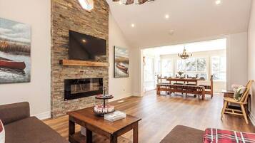 A spacious living room with a stone fireplace, a flat-screen TV, and a dining area with a wooden table and chairs.