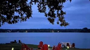 Un espace de détente aménagé au bord du lac, avec des chaises et des tables Adirondack rouges, entouré d’arbres et offrant une vue sur le lac.