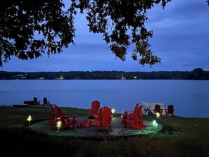 Een zitgedeelte aan het meer met rode Adirondack stoelen en tafels, omringd door bomen en uitzicht op het meer.