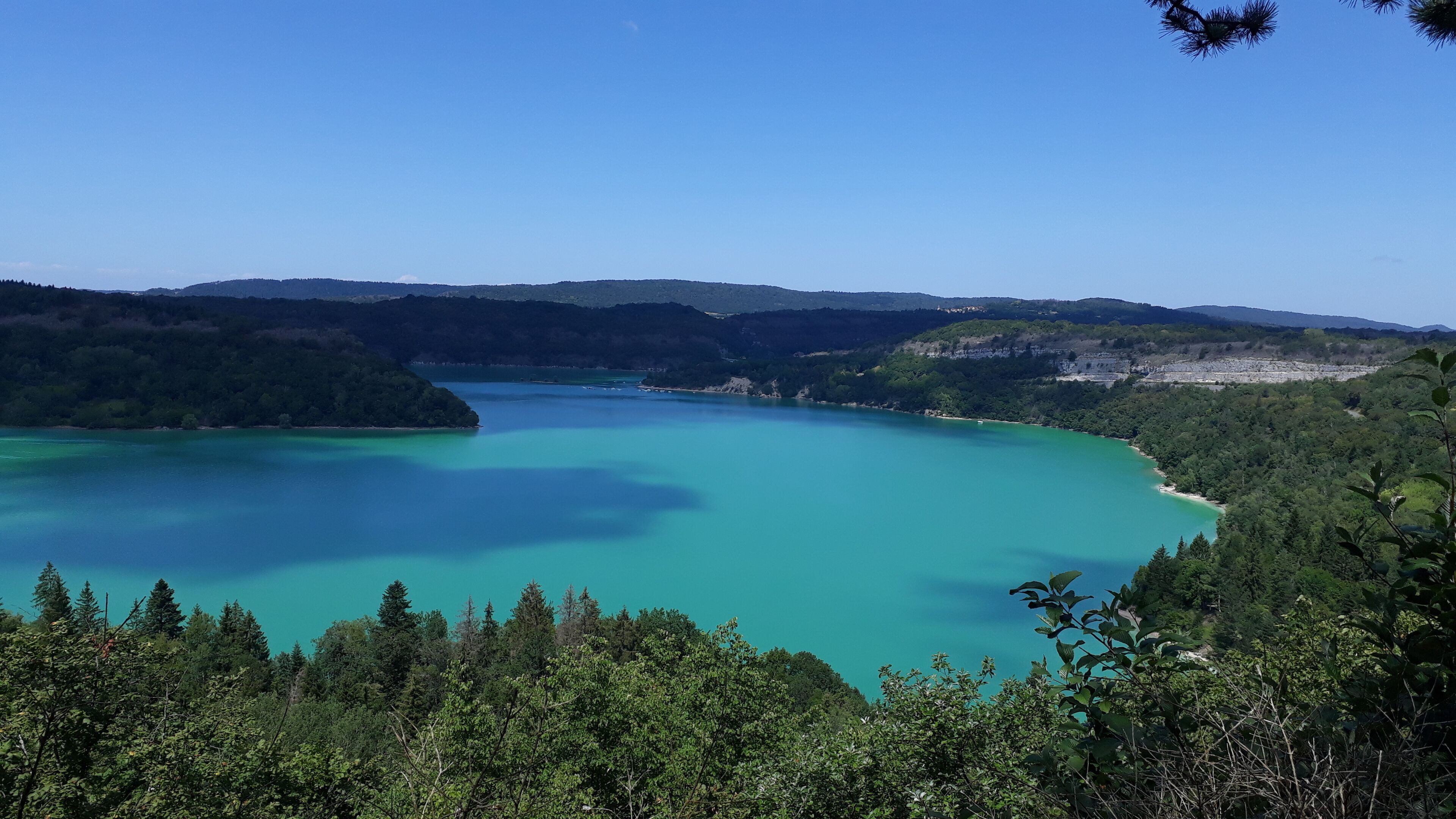 Vista panorámica de un lago turquesa rodeado de bosque denso y colinas.