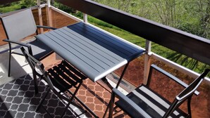 A balcony with a table and chairs, overlooking a green landscape with trees and a path. - Insertion Dans la Nature (Lamoura)