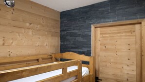 A bunk bed in a room with wooden walls and a dark stone accent wall. - Insertion Dans la Nature (Lamoura)