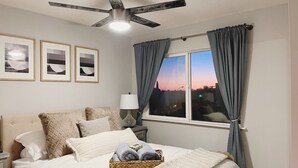 A bedroom with a bed, a ceiling fan, a window with curtains, and framed pictures on the wall. - Urban Escape: Trendy 1-Bed Condo with Balcony (San Diego)