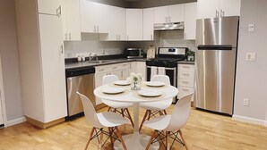 A modern kitchen with white cabinets, a stainless steel refrigerator, a stove, and a dining table with white chairs. - Urban Escape: Trendy 1-Bed Condo with Balcony (San Diego)