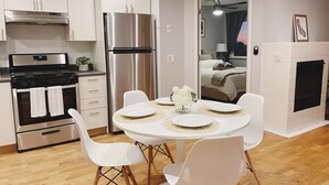 A modern kitchen with white cabinets, stainless steel appliances, and a dining area with a round table and white chairs. - Urban Escape: Trendy 1-Bed Condo with Balcony (San Diego)