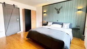 A modern bedroom with a large bed, wooden flooring, a sliding door, and a wall-mounted deer head decoration. - Hirschtraum im Zentrum von Braunlage (Braunlage)