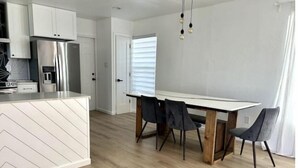 Eine moderne Küche mit weißen Schränken, einem Edelstahl-Kühlschrank und einem Essbereich mit einem Holztisch und vier Stühlen.