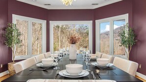 A dining room with a long table set for six, large windows, and two potted plants. - 7k SqFt Estate - Epic Amenities & Fun - Sleeps 20 (Biltmore Forest)