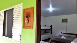 Quarto com uma cama de solteiro, uma cama individual, janela com persianas, ar condicionado fixado na parede e luminária no teto.
