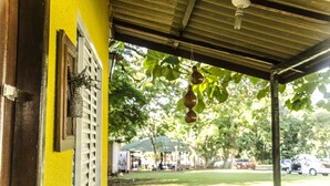 Um espaço ao ar livre coberto, com uma parede amarela, uma janela com uma planta decorativa e enfeites pendurados.