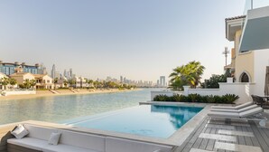 Una piscina en la azotea con vista al horizonte urbano, un área de descanso exterior blanca y una palmera.