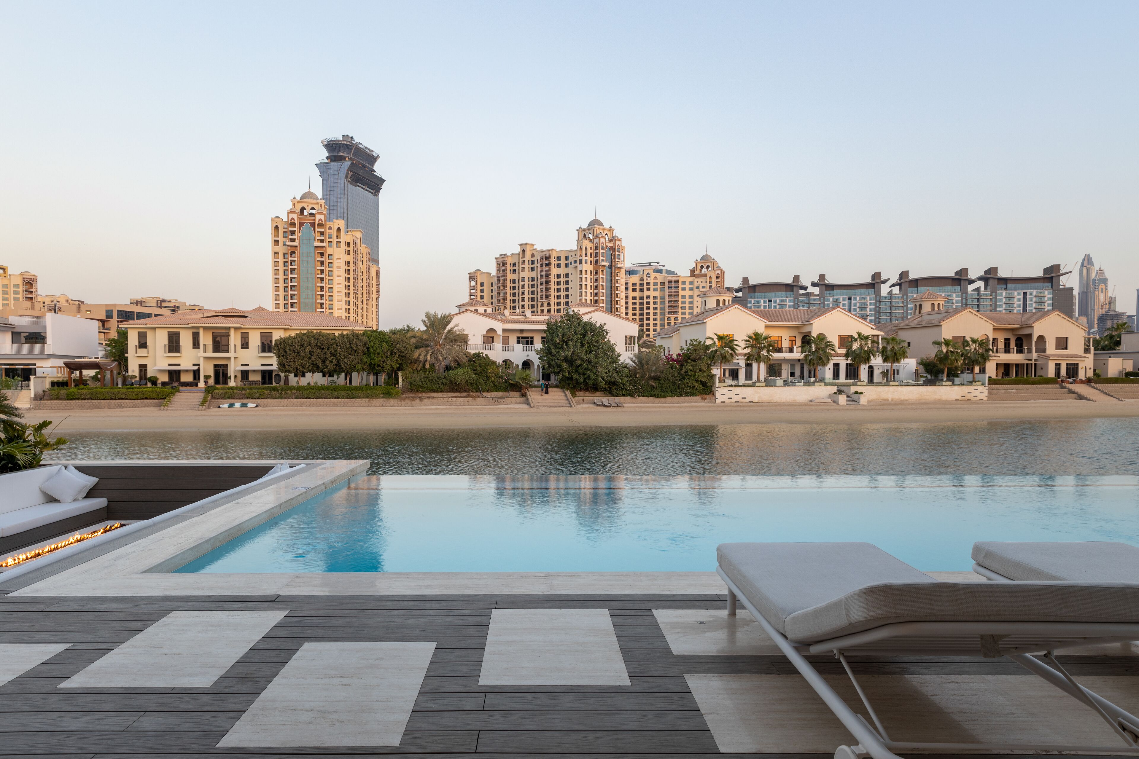 A swimming pool with lounge chairs, a wooden deck, and a view of high-rise buildings and a beach.