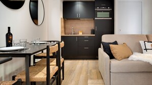 Una cocina compacta con armarios oscuros, un comedor con una mesa dispuesta para dos personas, y un sofá con una manta suave.