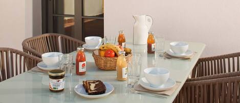 A breakfast table set with white bowls, plates, and a wicker chair.