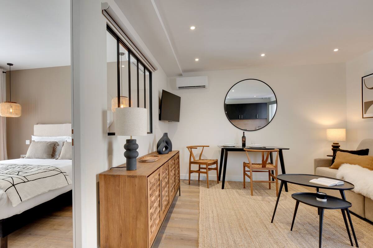 A modern hotel room with a bed, a wooden console, a dining area, and a sofa.