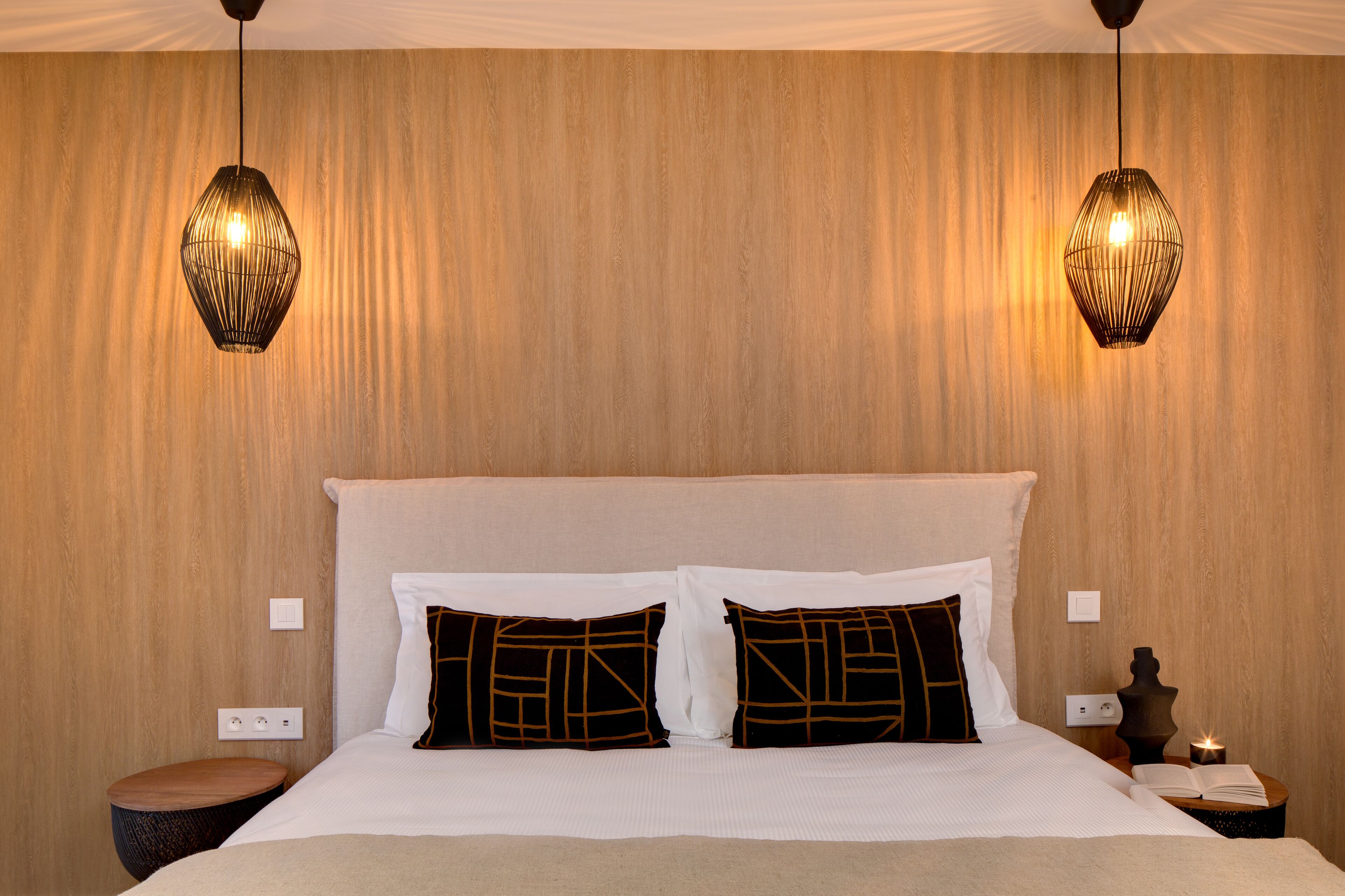 Habitación de hotel con una cama grande, dos mesitas de noche y dos lámparas colgantes.