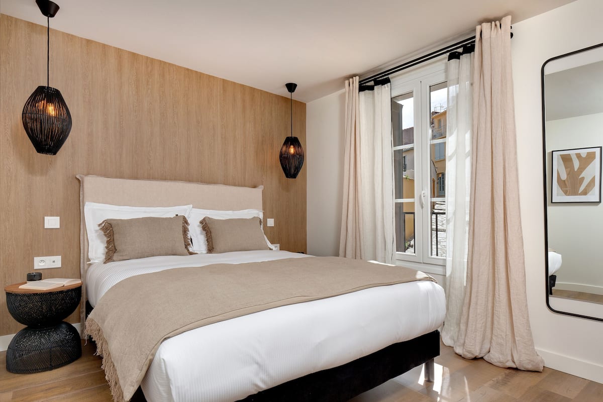 A bedroom with a bed, bedside tables, a window with curtains, and a mirror.