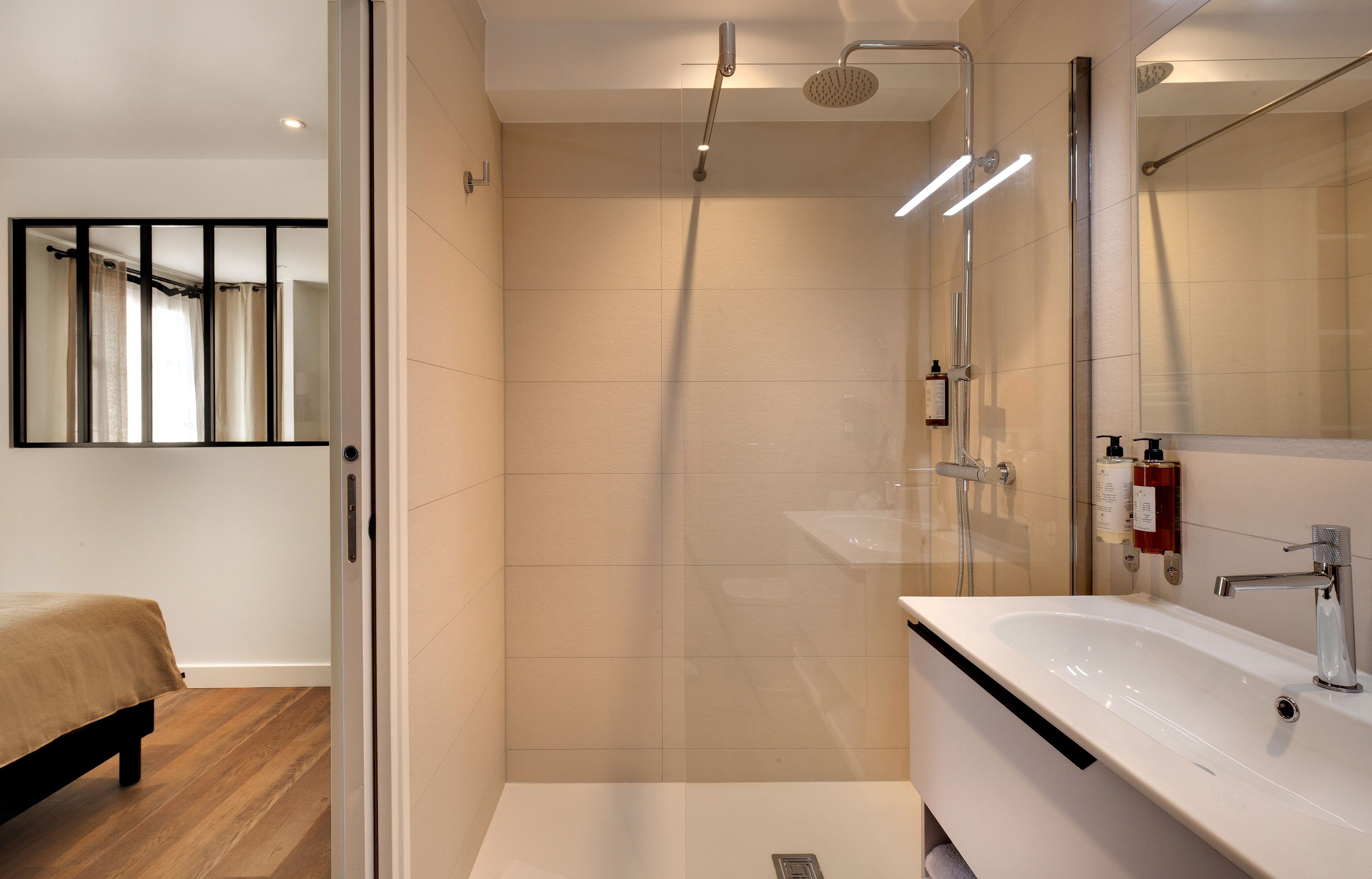 A modern bathroom with a glass shower enclosure, a white sink, and a large mirror.