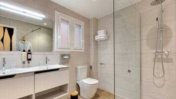 Un baño moderno con ducha envuelta en vidrio, inodoro blanco y tocador con espejo.