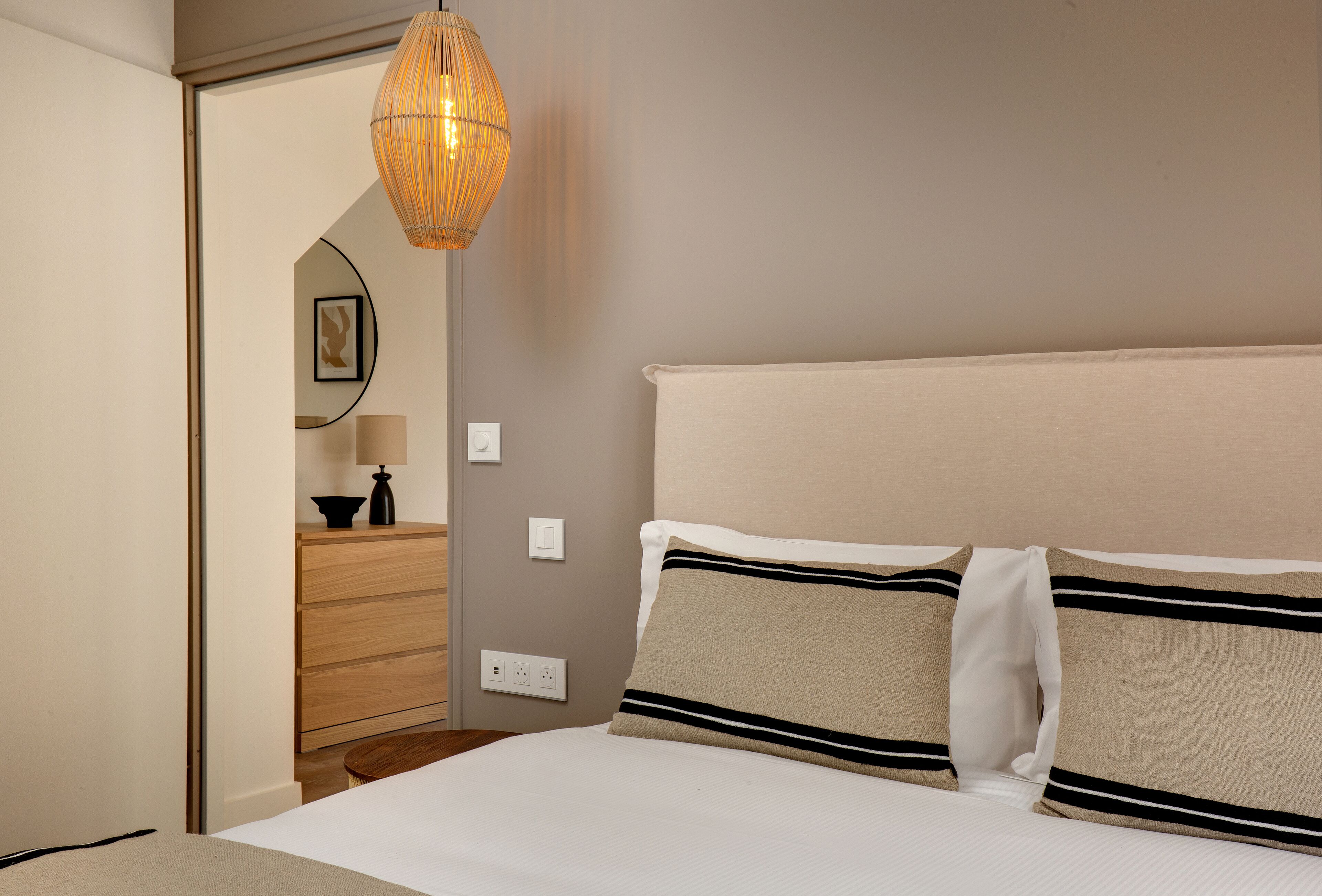 Une chambre bien rangée, avec un lit, une commode, un miroir et un luminaire suspendu.