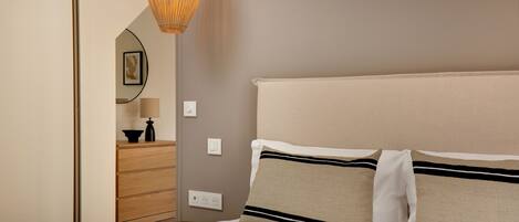 Une chambre bien rangée, avec un lit, une commode, un miroir et un luminaire suspendu.
