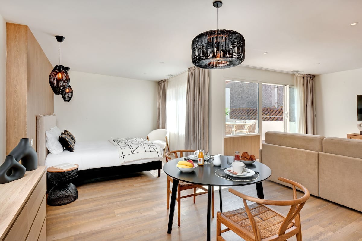 A modern hotel room with a bed, a dining area, a sofa, and a TV.