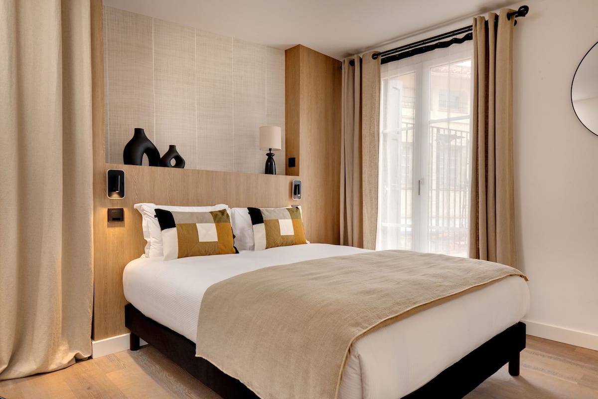A hotel room with a large bed, a bedside table, a mirror, and a window with curtains.