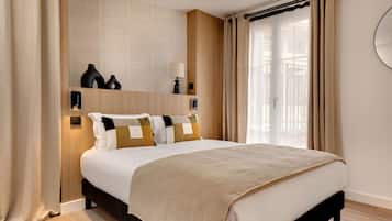 Quarto de hotel com cama grande, mesa de cabeceira, espelho e janela com cortinas.