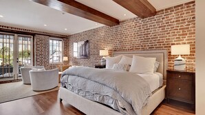 Ein Schlafzimmer mit einem großen Bett, zwei Nachttischen, einem Beistelltisch, einem Sessel und einer Ziegelwand.