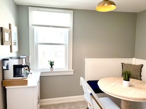 A compact kitchen with a coffee maker, a small potted plant, and a white cabinet.