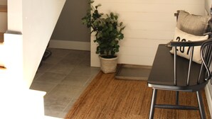 Een trap met houten leuning, een ronde spiegel aan de muur, een potplant, een kleine tafel met stoel, en een hangende tas.