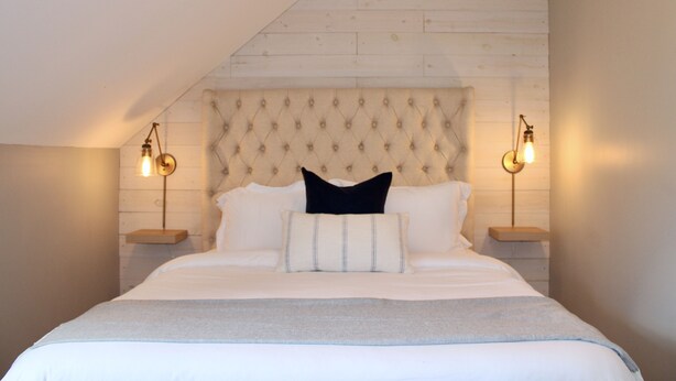 Een slaapkamer met een gestoffeerd hoofdeinde, twee bedlampen, en een bed met wit beddengoed en een zwart kussen.