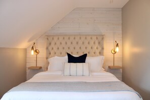 A bedroom with a tufted headboard, two bedside lamps, and a bed with white bedding and a black pillow.