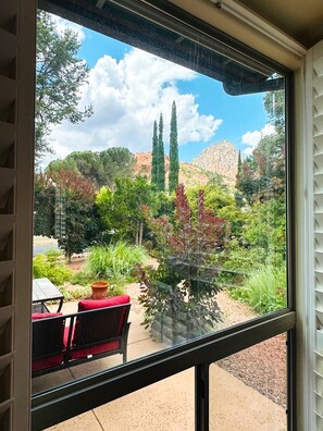 A view from a window with a patio area, including a table and chairs, and a variety of trees and shrubs. - Walk to Trails, Private Hot Tub, Red Rock Views, 3BR with 2 Kings, Sunset Deck (Sedona)